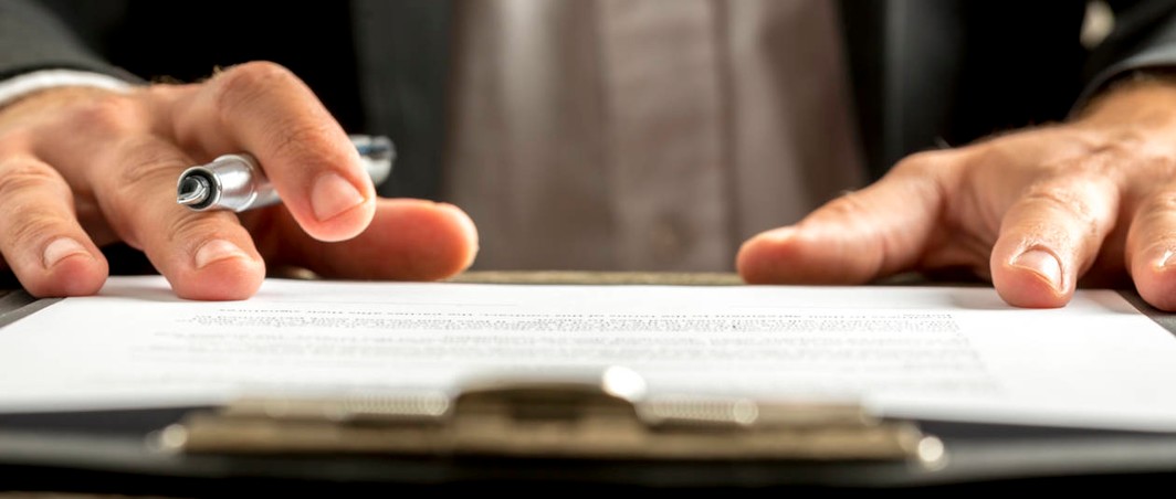 Two hands with pen, ready to sign document with terms and conditions